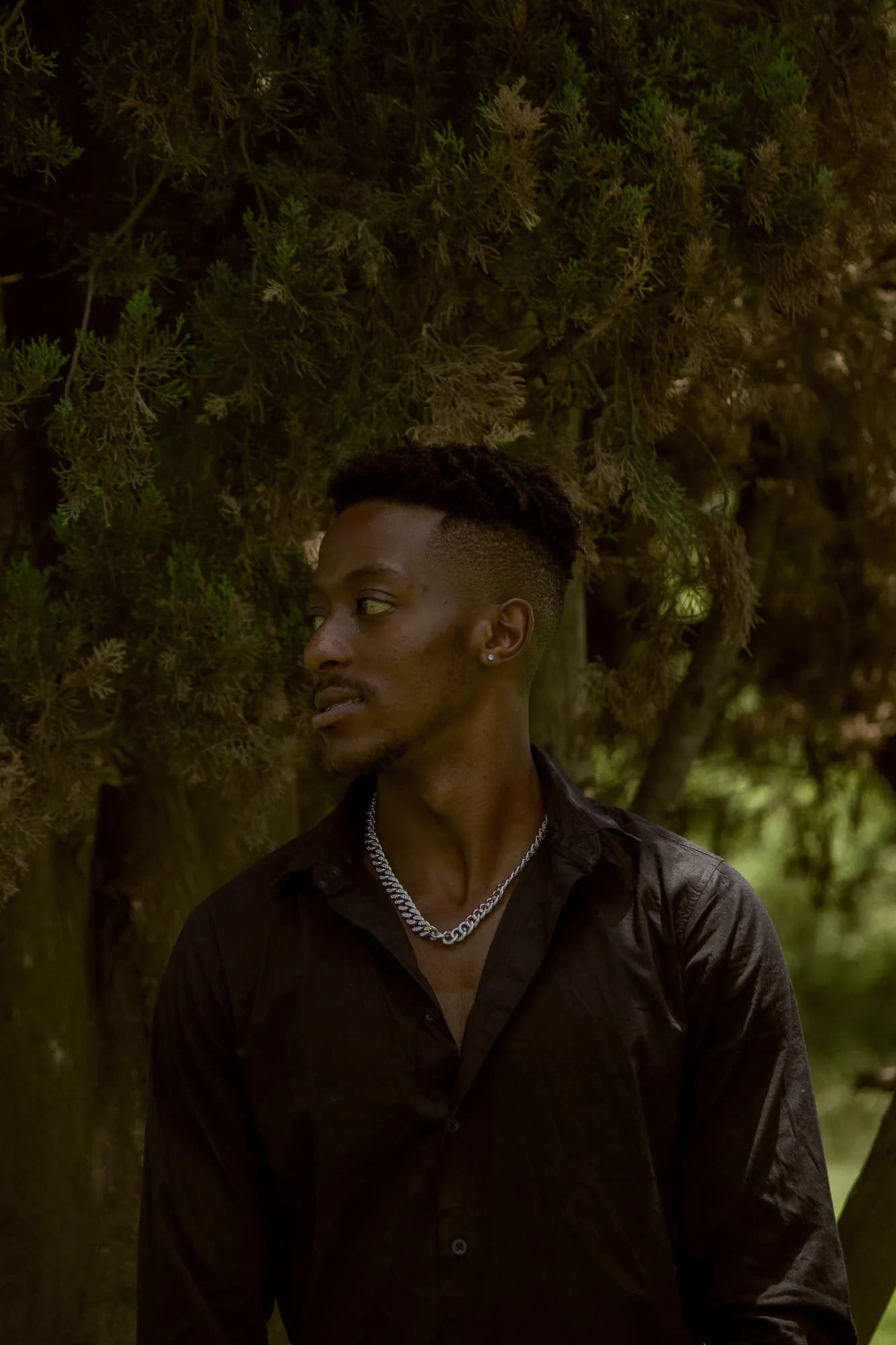 Portrait of Sihle in a dark shirt among leaves at dusk